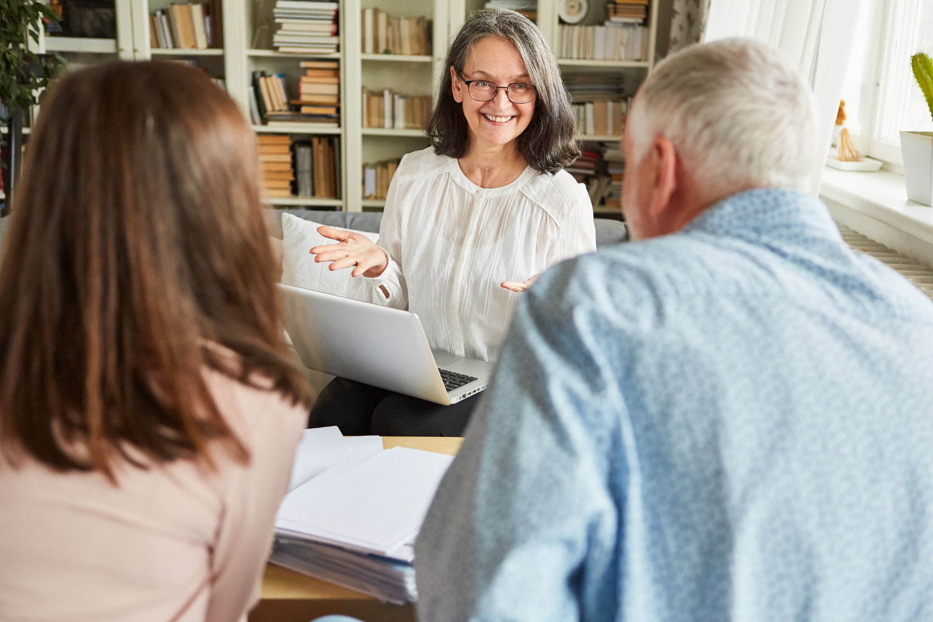 Three people in a bright office meeting, with a woman presenting at a laptop and smiling.