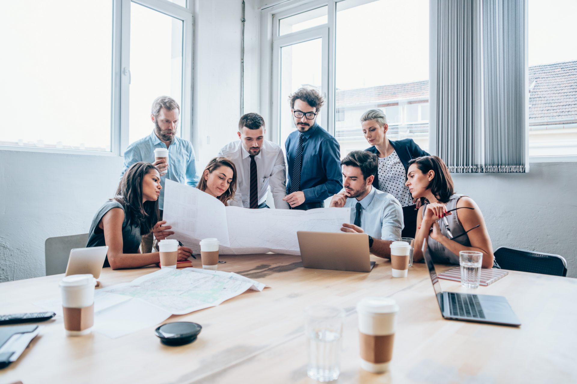 Team reviewing documents around a laptop in a bright office conference room