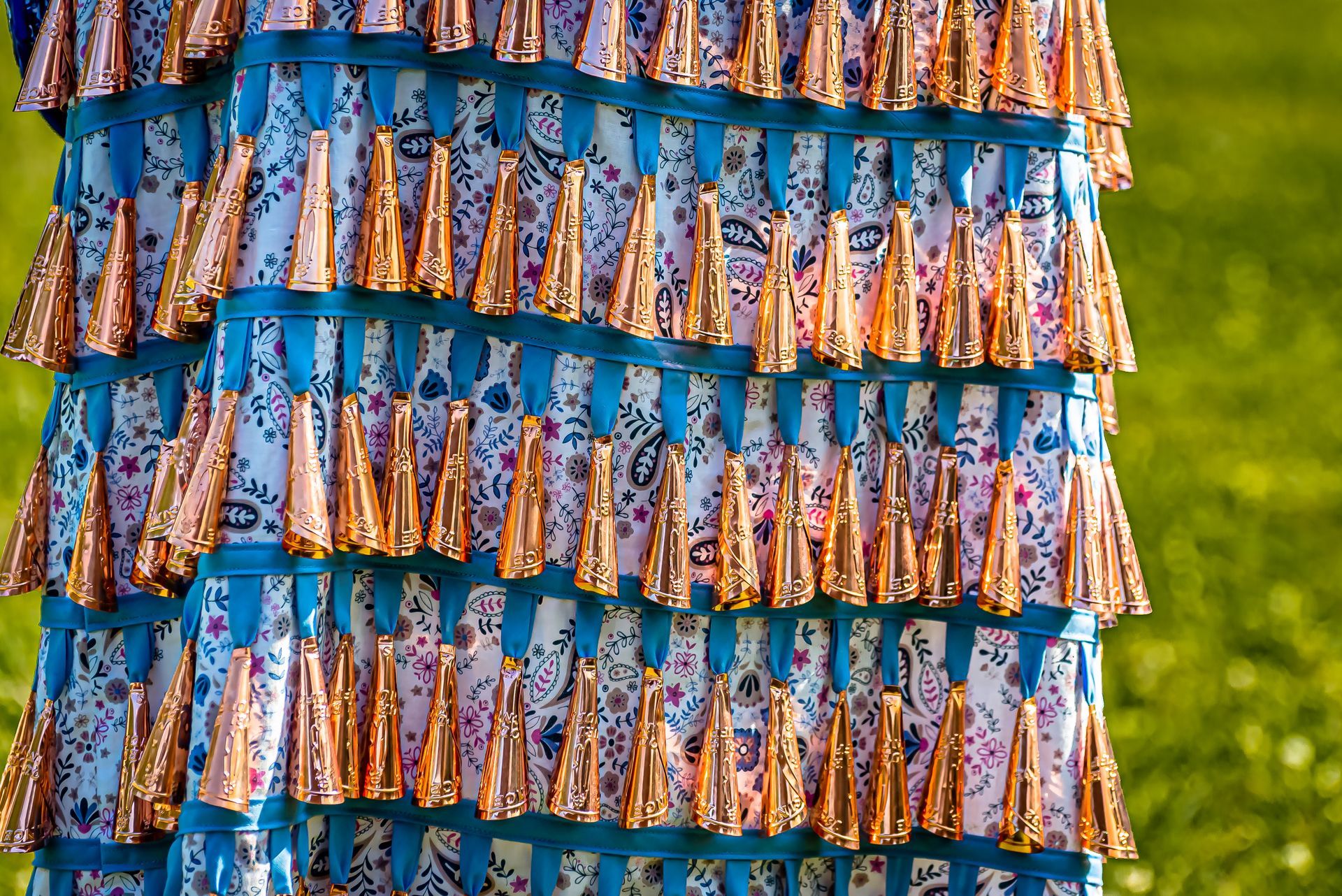 Rows of colorful patterned fabric strips hanging outdoors against a green background