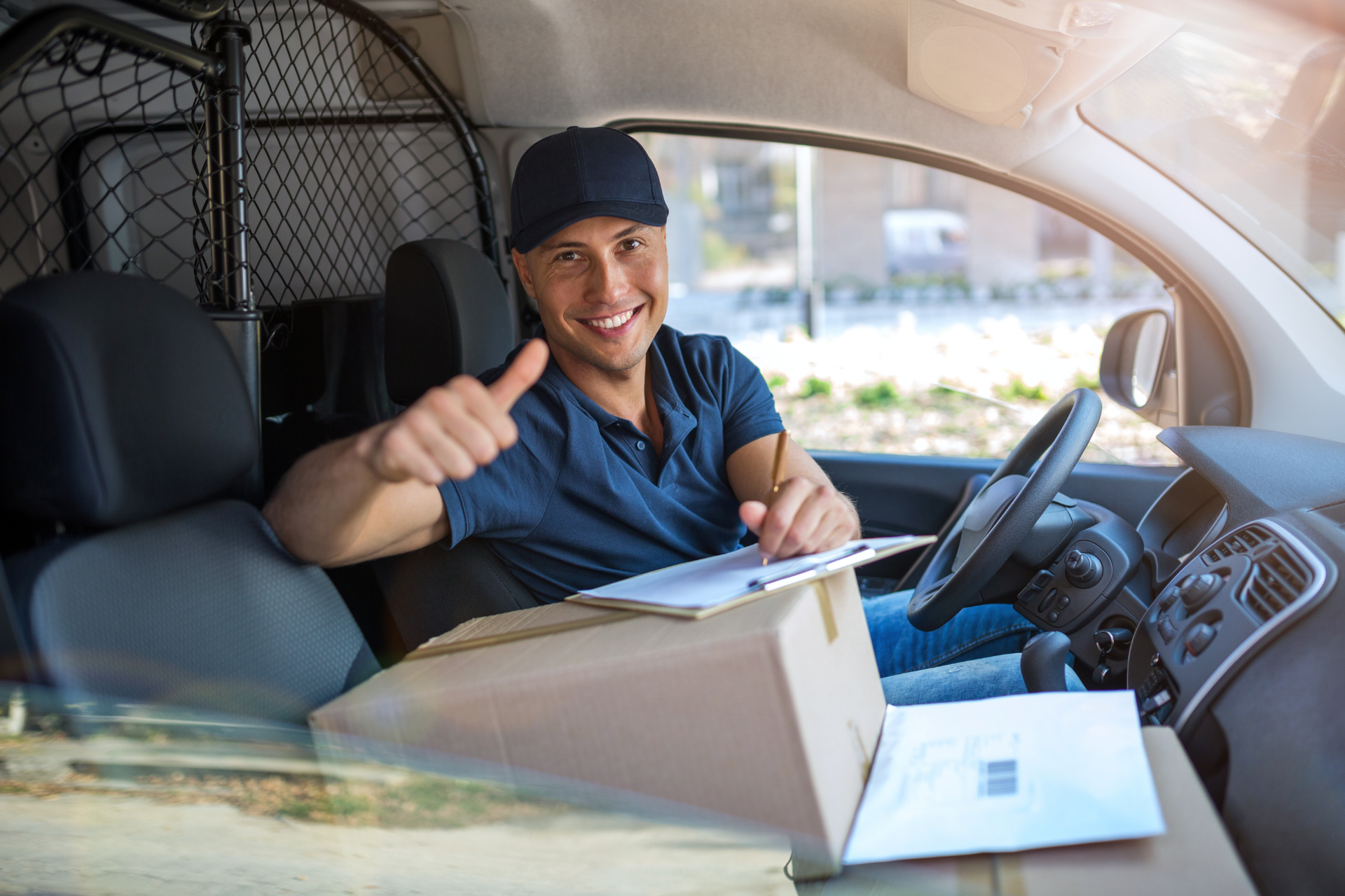 Smiling delivery driver in a van holding a clipboard and giving a thumbs-up