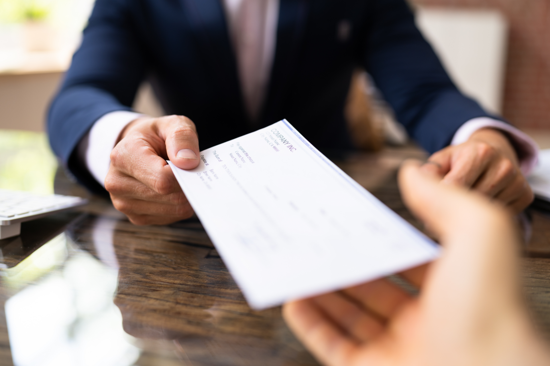 Person in a suit handing a white check across a wooden table