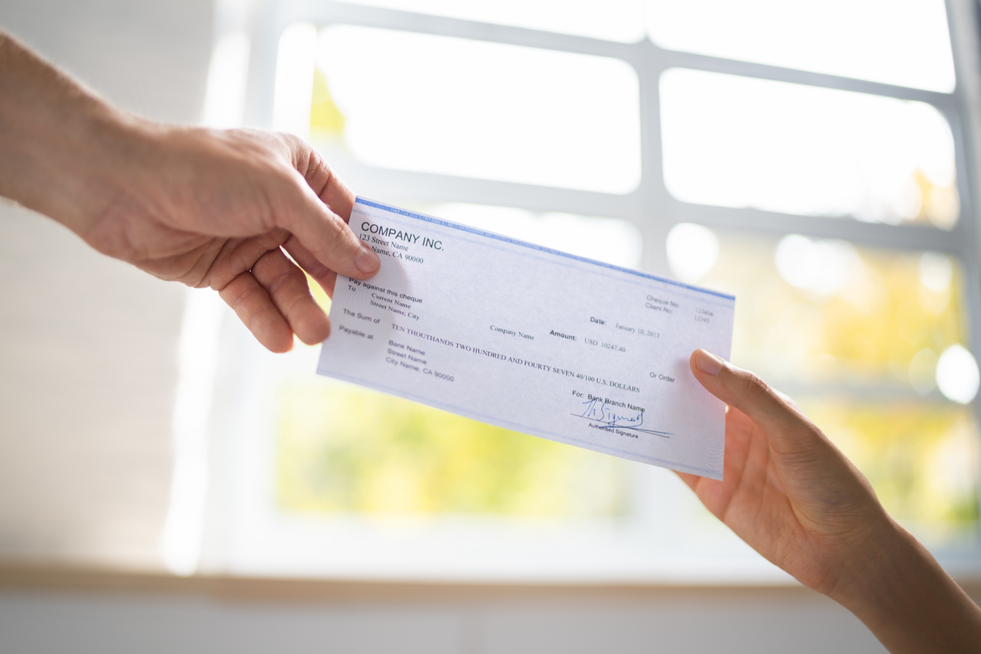 Two hands exchanging a blank check in front of a bright window