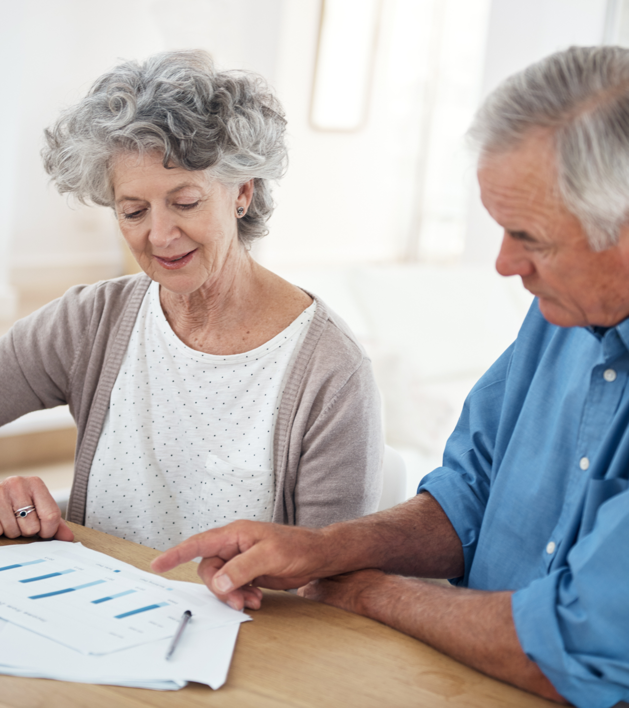 Two older adults reviewing papers at a table, one pointing to a document.