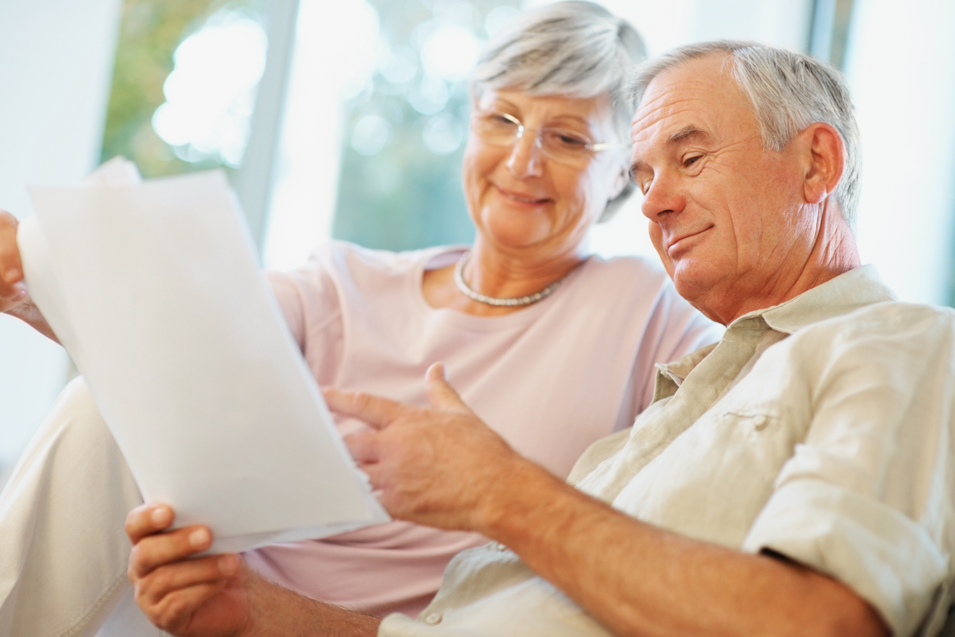 Older couple reading a document together on a couch in a bright room