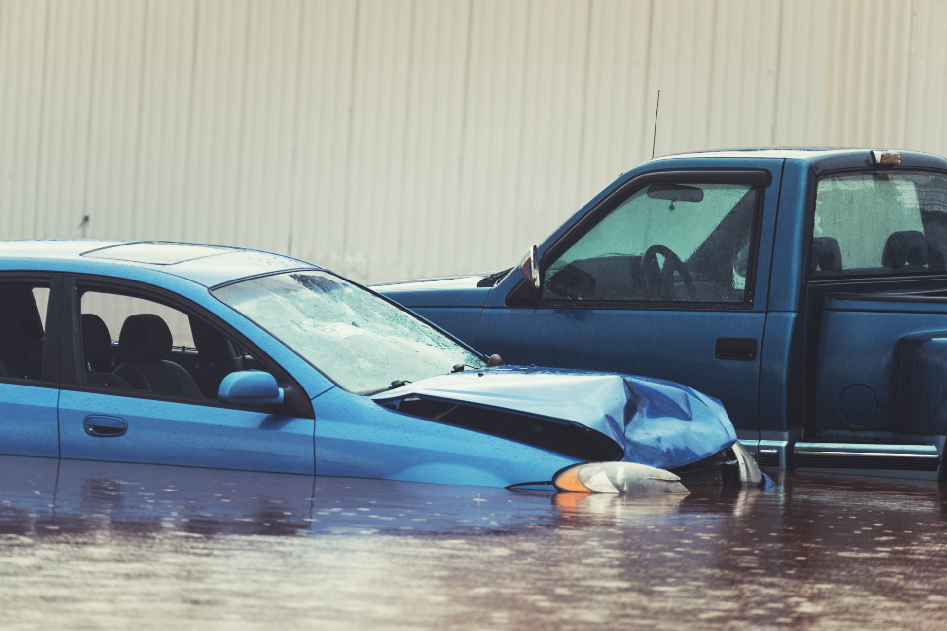 Two cars partly submerged in floodwater beside a beige building