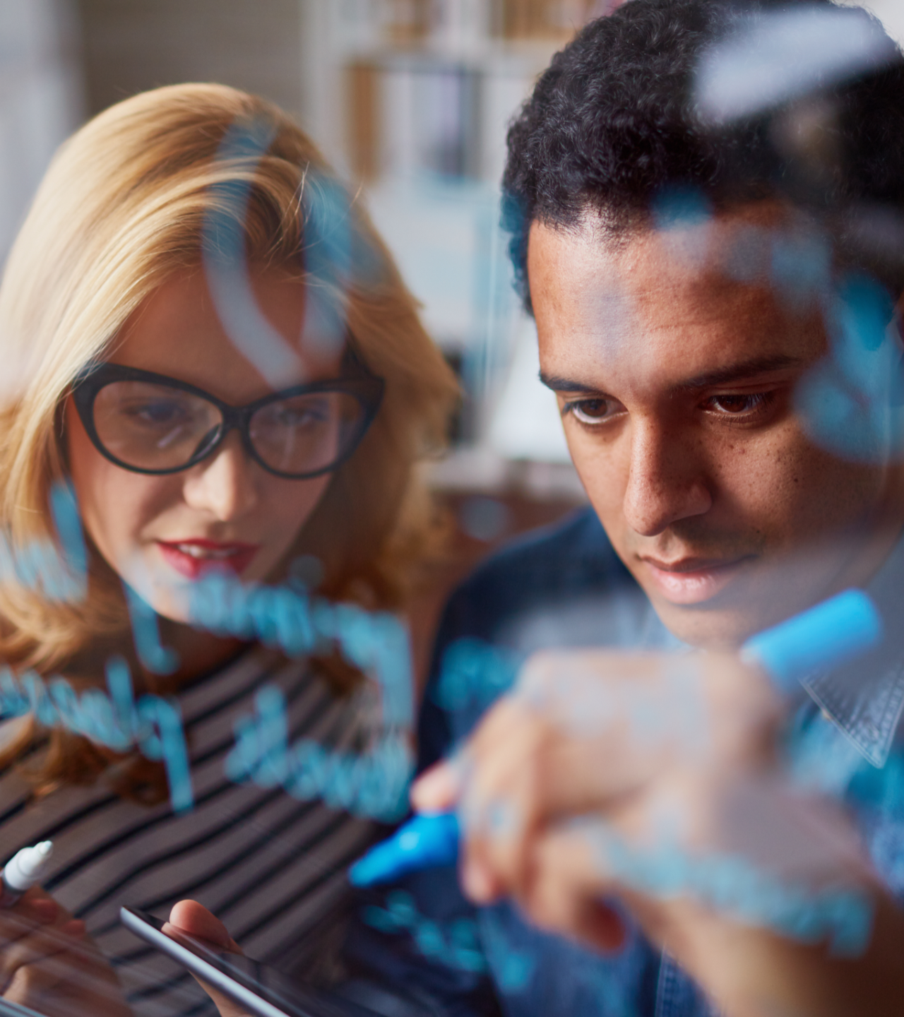 Two people collaborating on a tablet behind a transparent screen with blue code projections