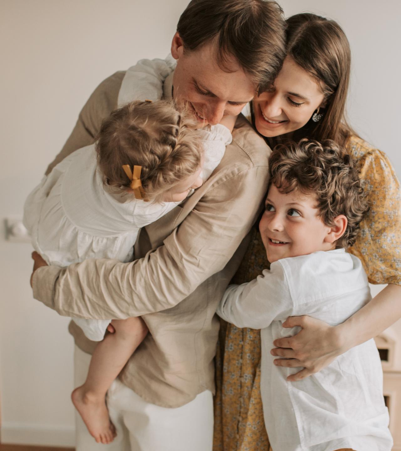 Family of four hugging and smiling in a warm indoor embrace