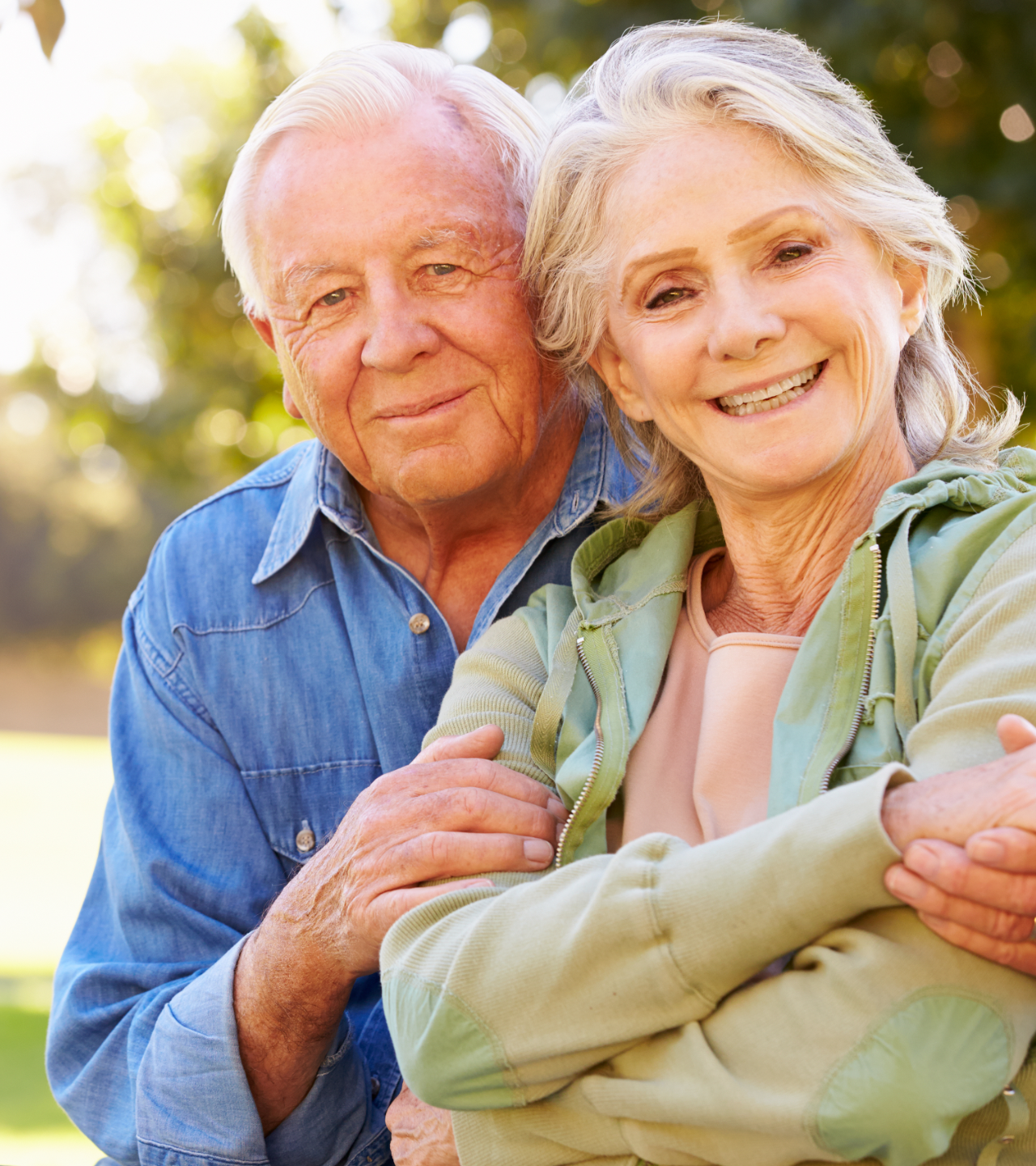 Two smiling people outdoors, embracing in warm sunlight with greenery in the background