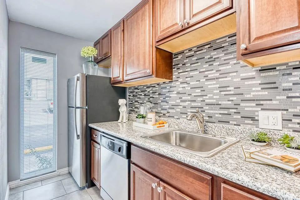 Modern kitchen with wooden cabinets, stainless appliances, mosaic tile backsplash, and a granite countertop near a glass door