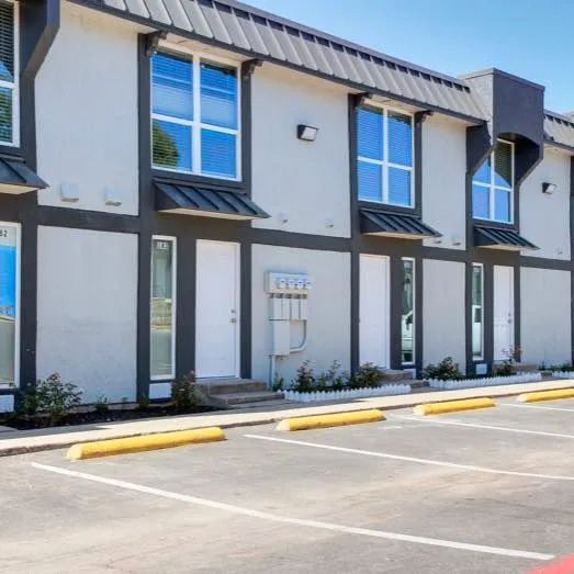 Modern gray townhouses with large windows and yellow parking curbs in a sunny lot