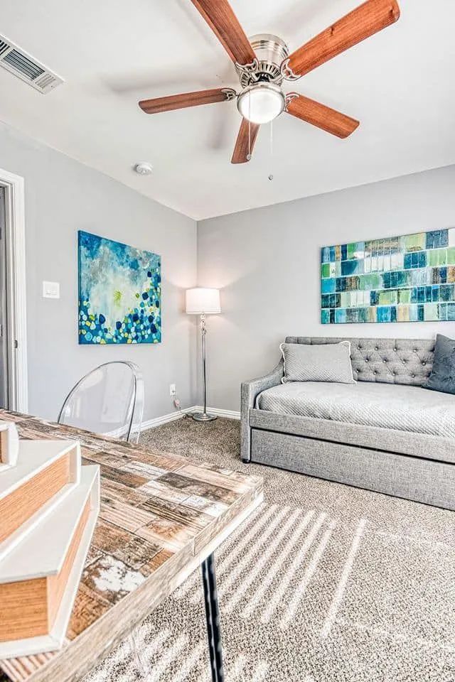 Bright gray living room with ceiling fan, gray sofa, floor lamp, and colorful wall art