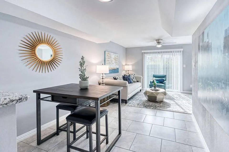 Bright modern dining area with a dark table, bar stools, wall mirror, and sliding glass doors to a balcony