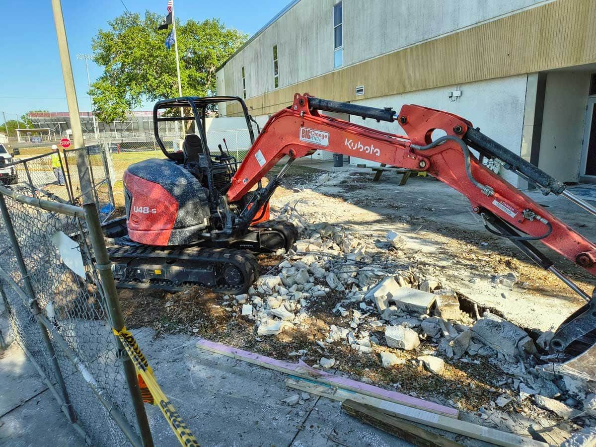 Red excavator clearing debris beside a building on a construction site