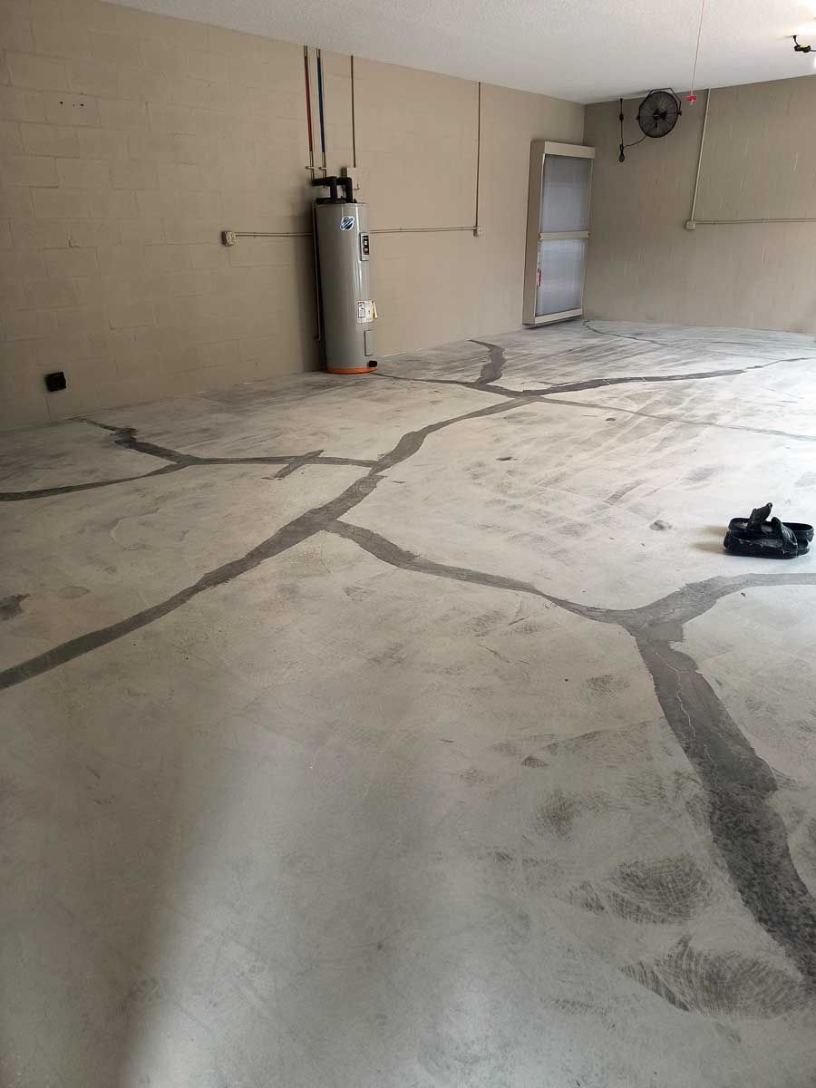 Empty garage with repaired cracked concrete floor and a water heater against the wall. Prepped floor for first layer of epoxy.