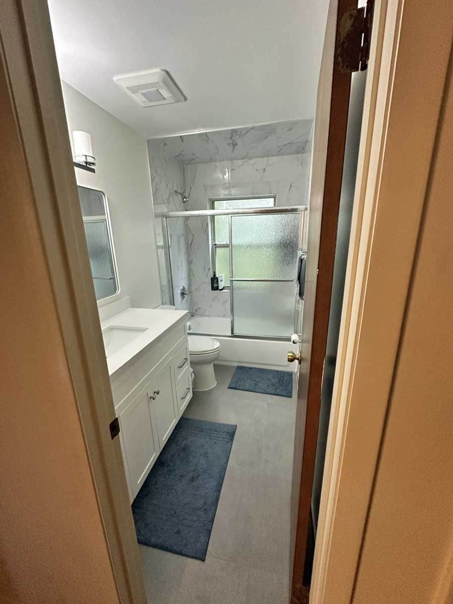 Bright bathroom with white vanity, blue rugs, and a glass shower enclosure.