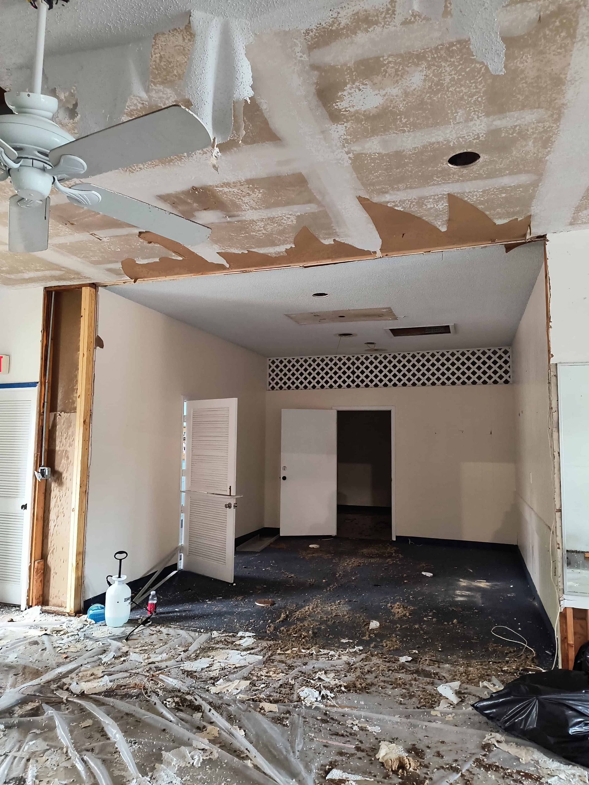 Demolished interior room with torn ceiling, debris on floor, open doorway, and exposed framing.