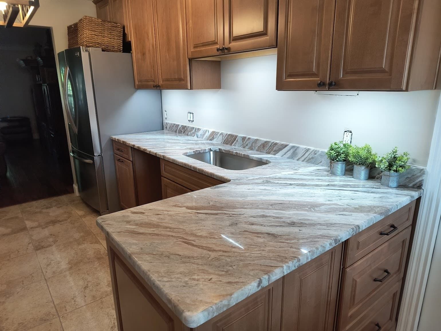 Modern kitchen with wood cabinets, stainless refrigerator, and a large white-and-gray marble countertop