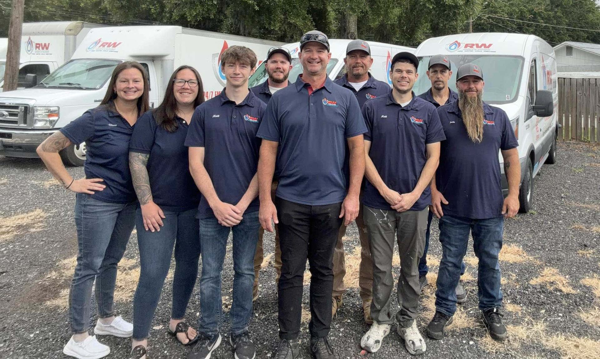 The RW Services team in navy shirts standing in front of white service vans on a wet lot