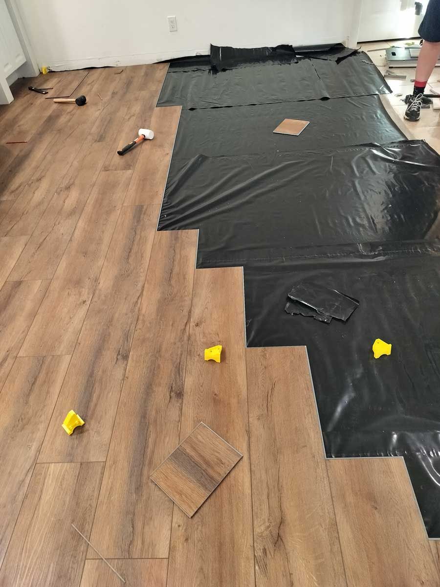 Wood-look floor underlayment with black protective sheeting and yellow spacers in a room under renovation