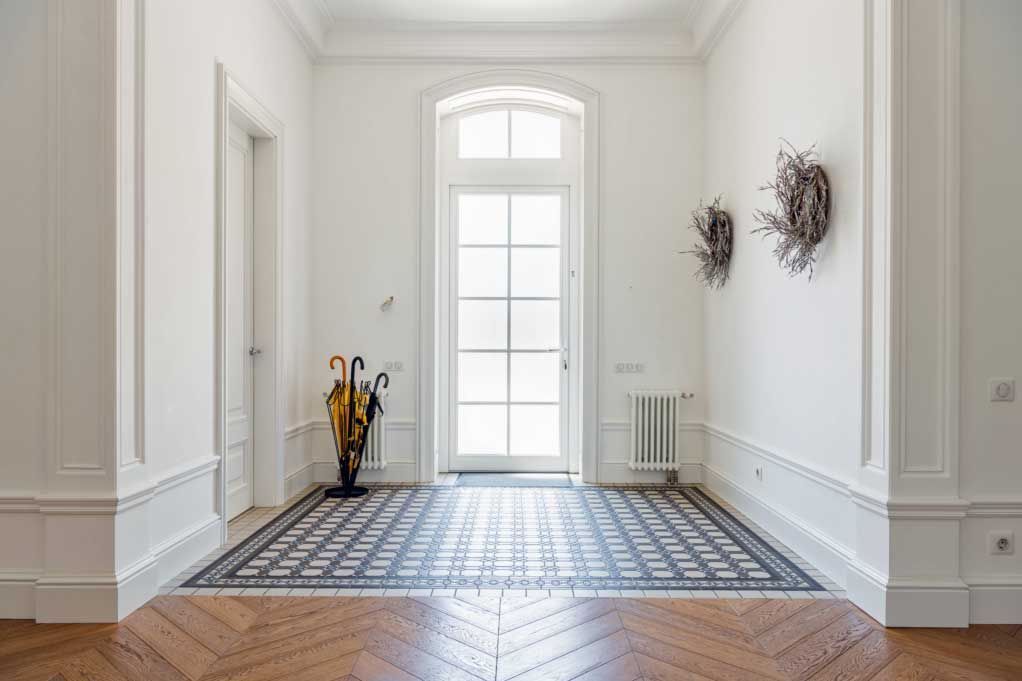 Bright hallway with tiled rug, white walls, tall windowed door, and yellow umbrella stand