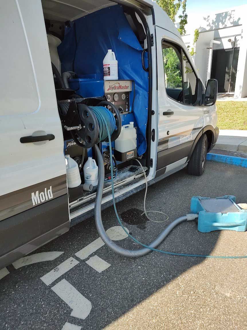 Industrial cleaning machine mounted on white van, with hoses and blue equipment on roadside.