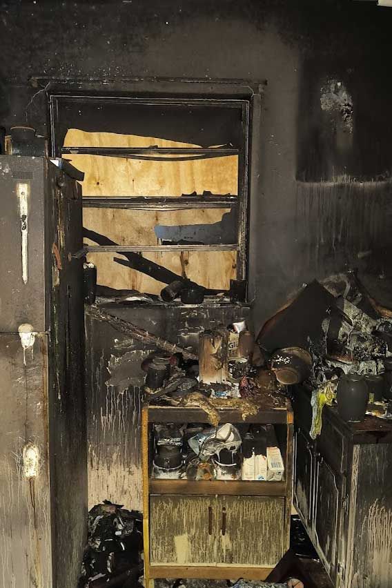 Fire-damaged room with blackened walls, burned doorway, and charred furniture amid heavy smoke damage