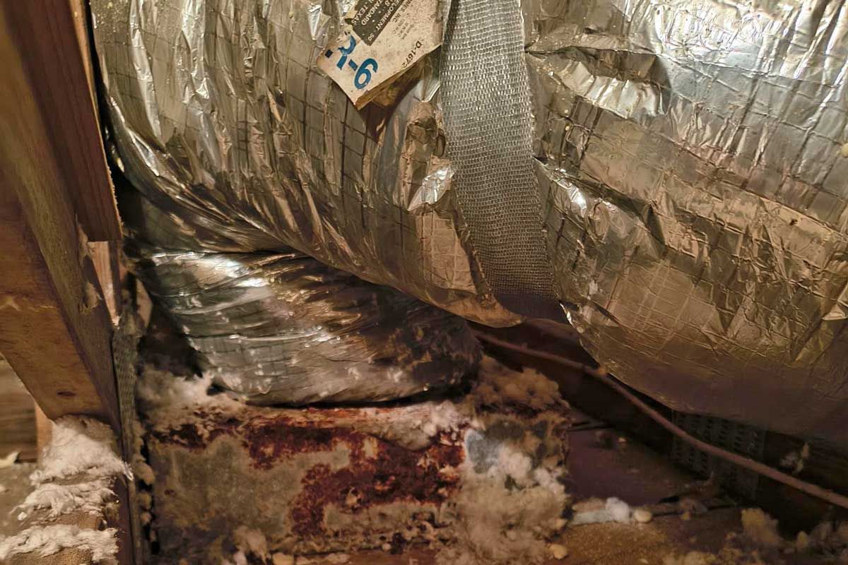 Attic ductwork with insulation, rust, and moisture stains.