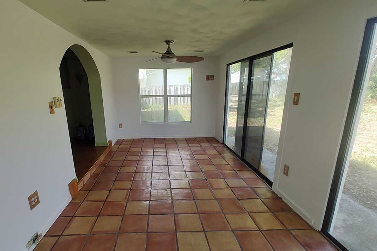 Empty tiled sunroom with arched doorway, ceiling fan, and sliding glass doors overlooking greenery