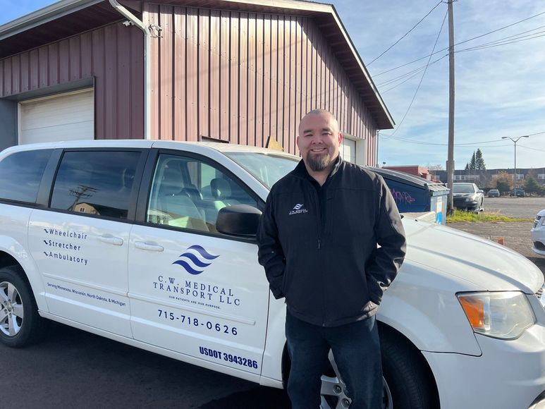 A man in a black jacket is standing in front of a white van.