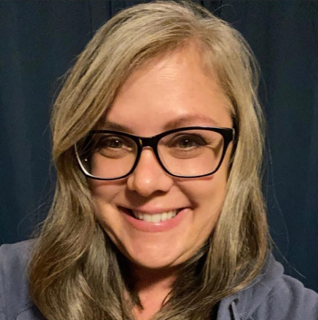 A smiling person with shoulder-length light hair wears black-rimmed glasses, positioned against a dark blue background.
