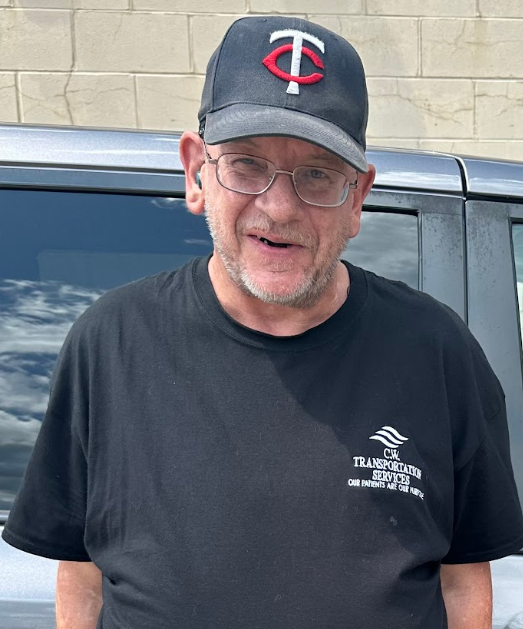 A person wearing a black Minnesota Twins baseball cap and a black t-shirt standing in front of a gray vehicle.