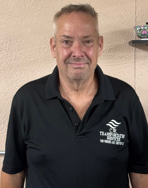 A person wearing a black C.W. Transportation Services polo shirt stands smiling against a textured tan wall.
