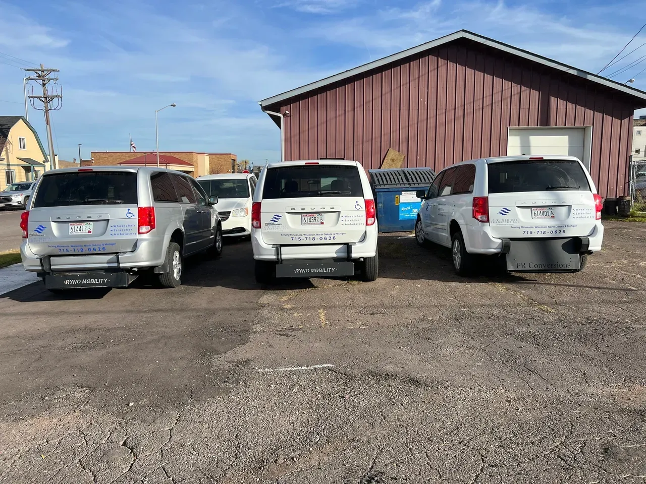 Three white vans are parked in a gravel lot in front of a building.