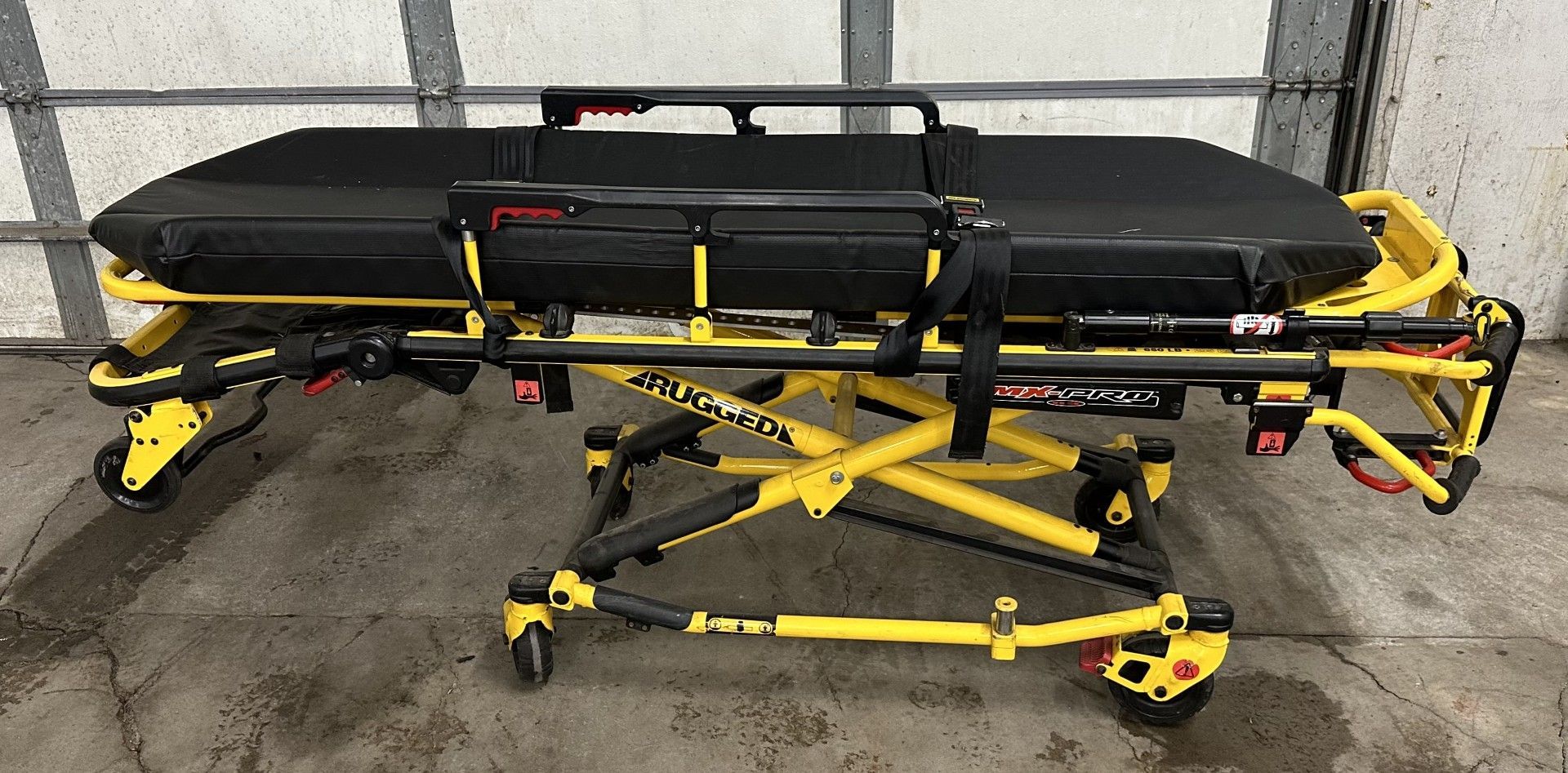 A black and yellow stretcher with wheels is sitting in front of a garage door.