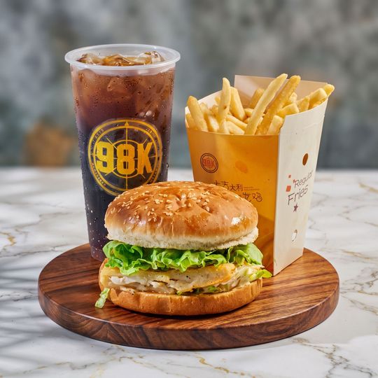 Burger, fries, and a soda on a wooden tray atop a marble table.