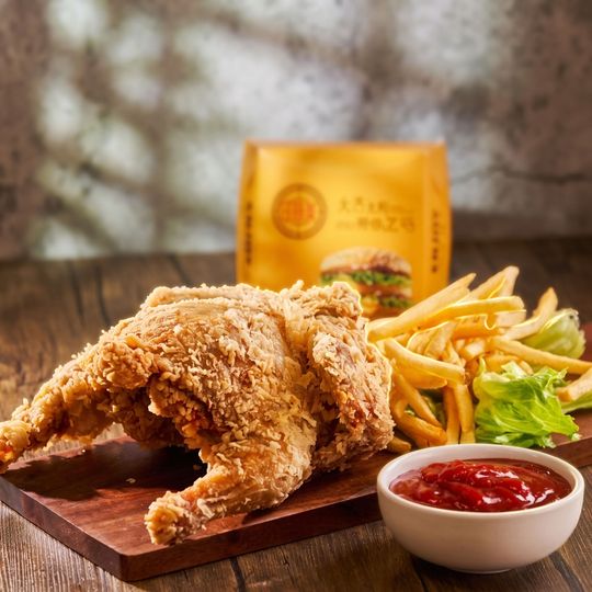 Crispy fried chicken with fries and ketchup on a wooden board, with a yellow bag in the background
