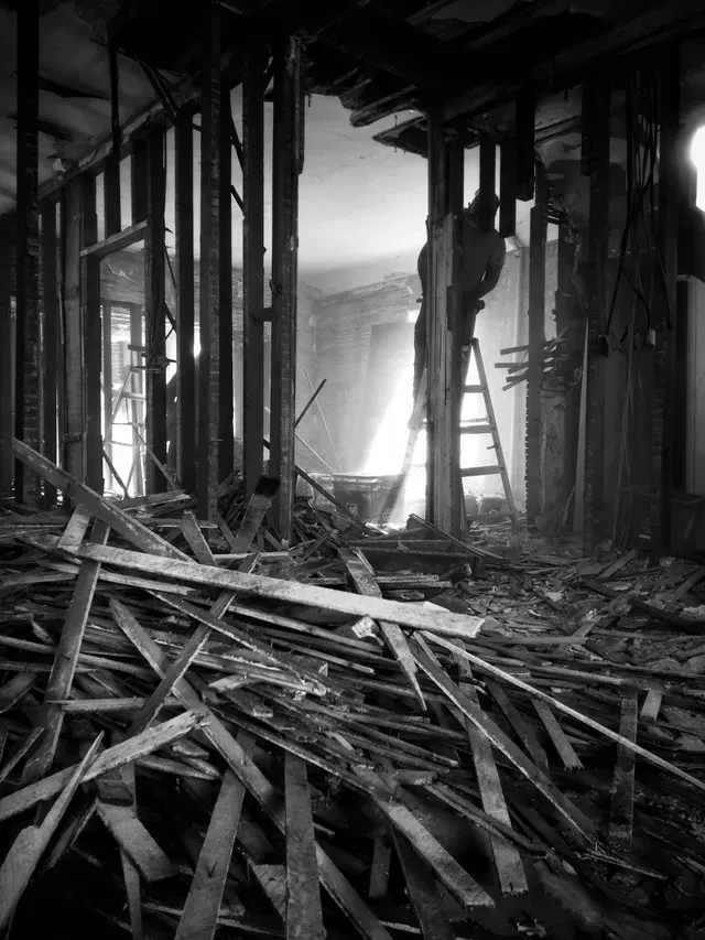 A black and white photo of a building under construction with a pile of wood.