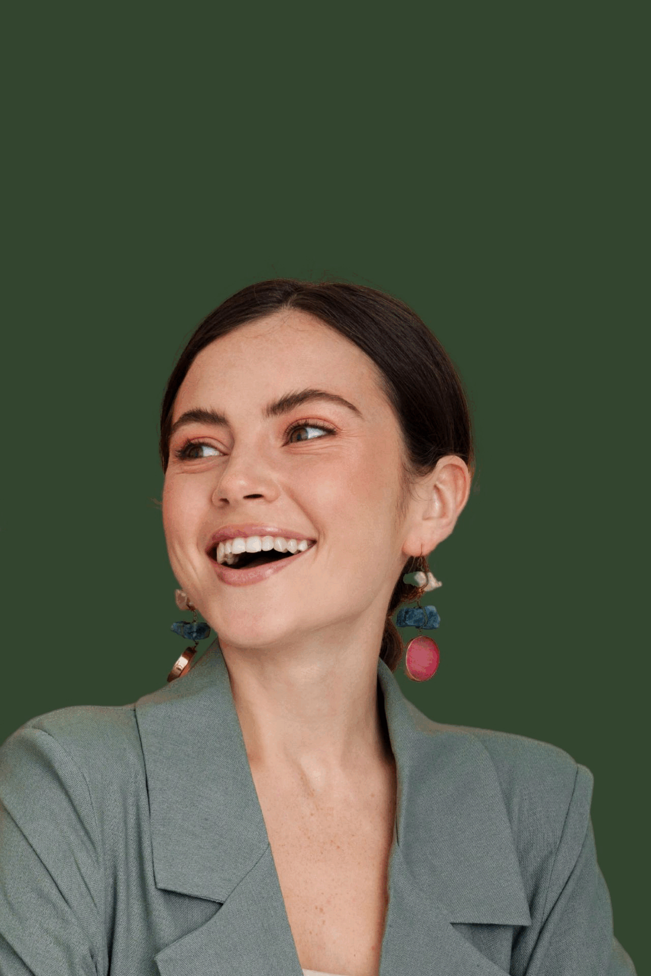 A woman in a suit and earrings is smiling on a yellow background.