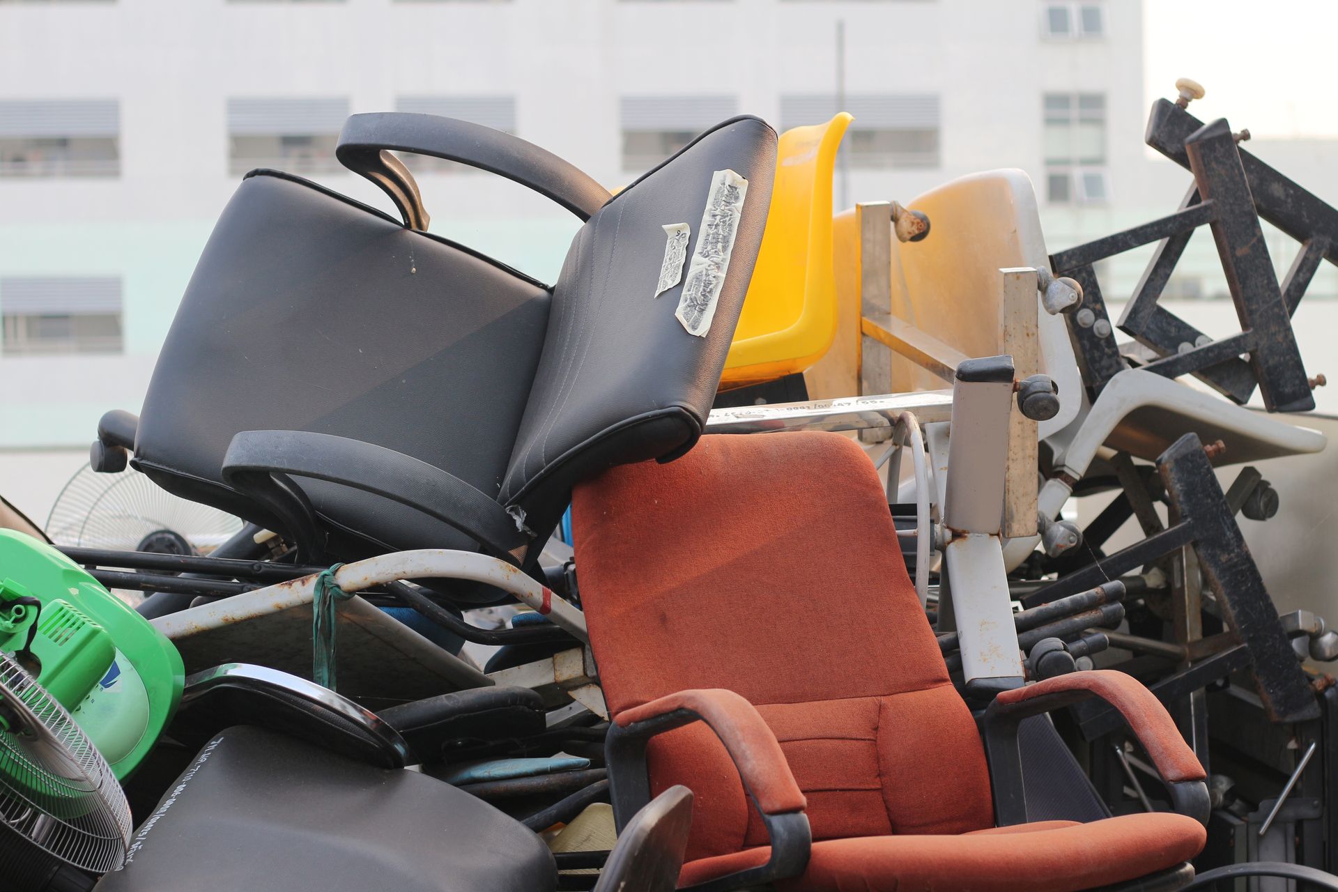 Pile of discarded office chairs in various colors, outdoors.