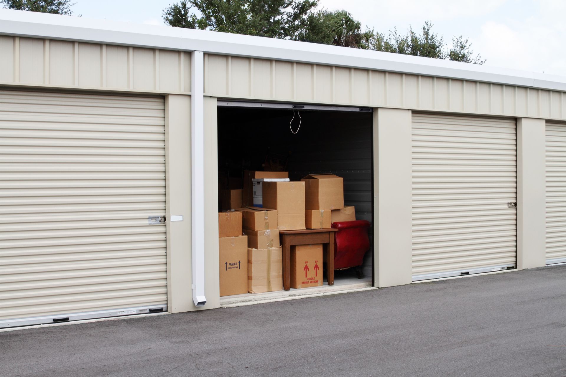 Storage unit with tan metal doors, one open revealing stacked cardboard boxes and furniture.