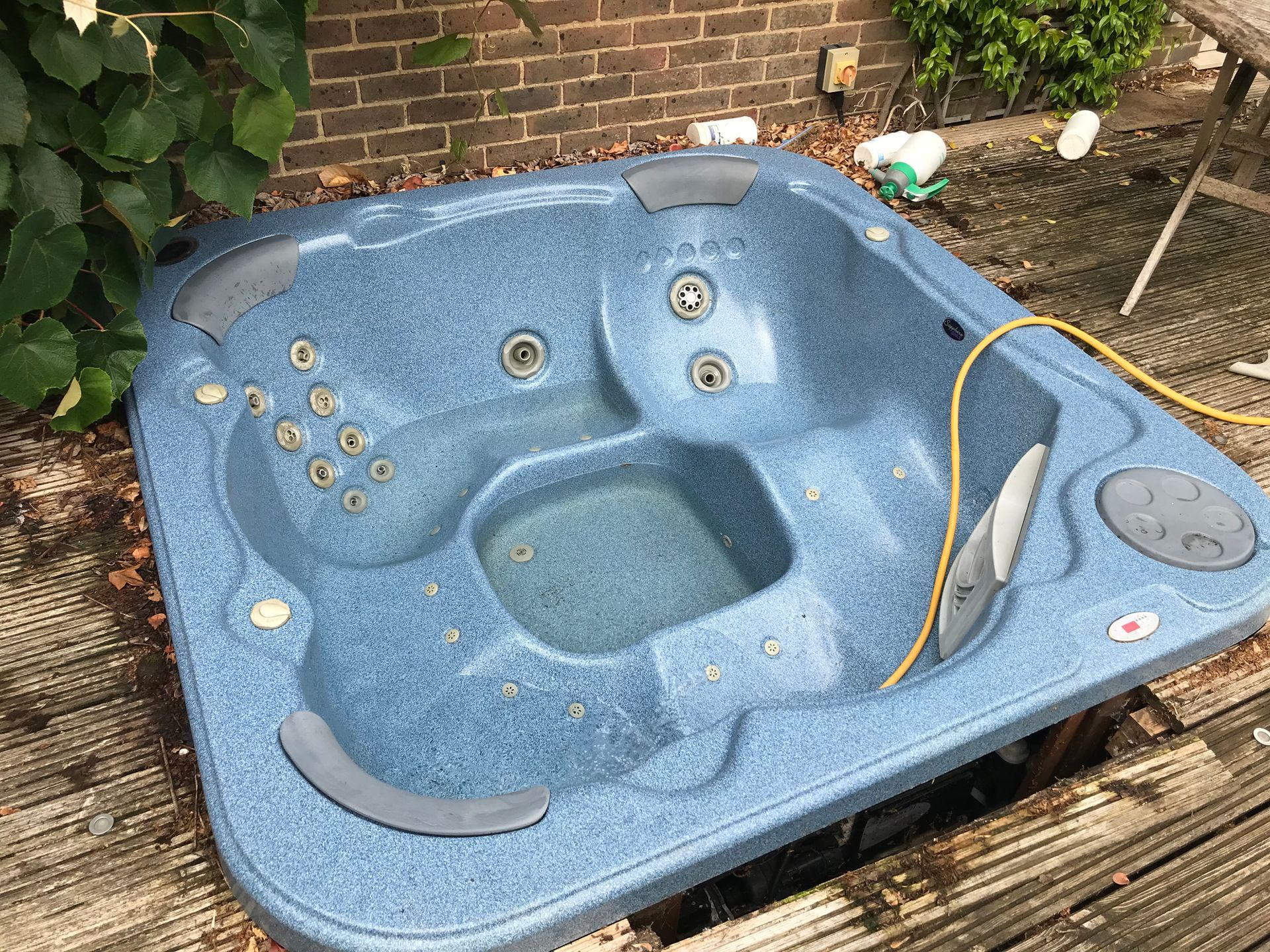 Blue speckled hot tub on a wooden deck next to a brick wall. 