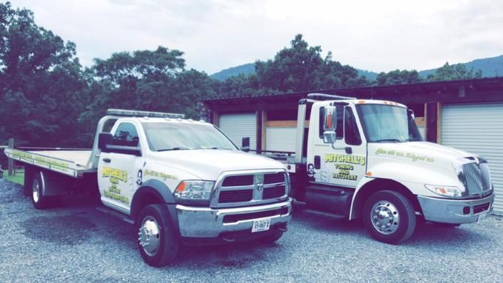 Two tow trucks parked on a gravel lot, one white pickup-style and one white semi truck.