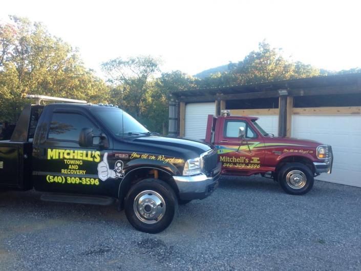 Two Mitchell’s service trucks parked outside a garage, one black and one red, with company lettering.