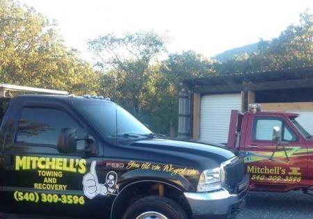 Tow black Mitchell's Towing & Recovery trucks parked outside a garage in daylight
