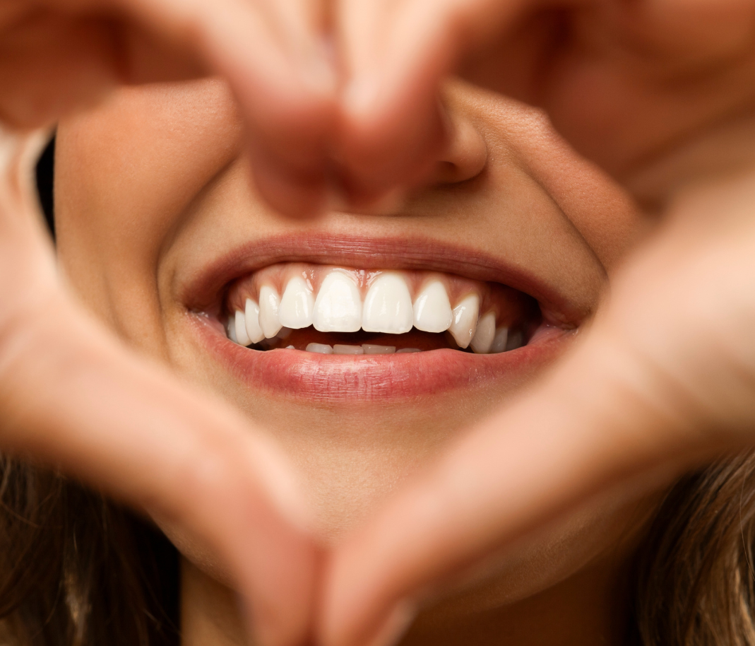 Close-up of a smiling mouth framed by hands forming a heart shape