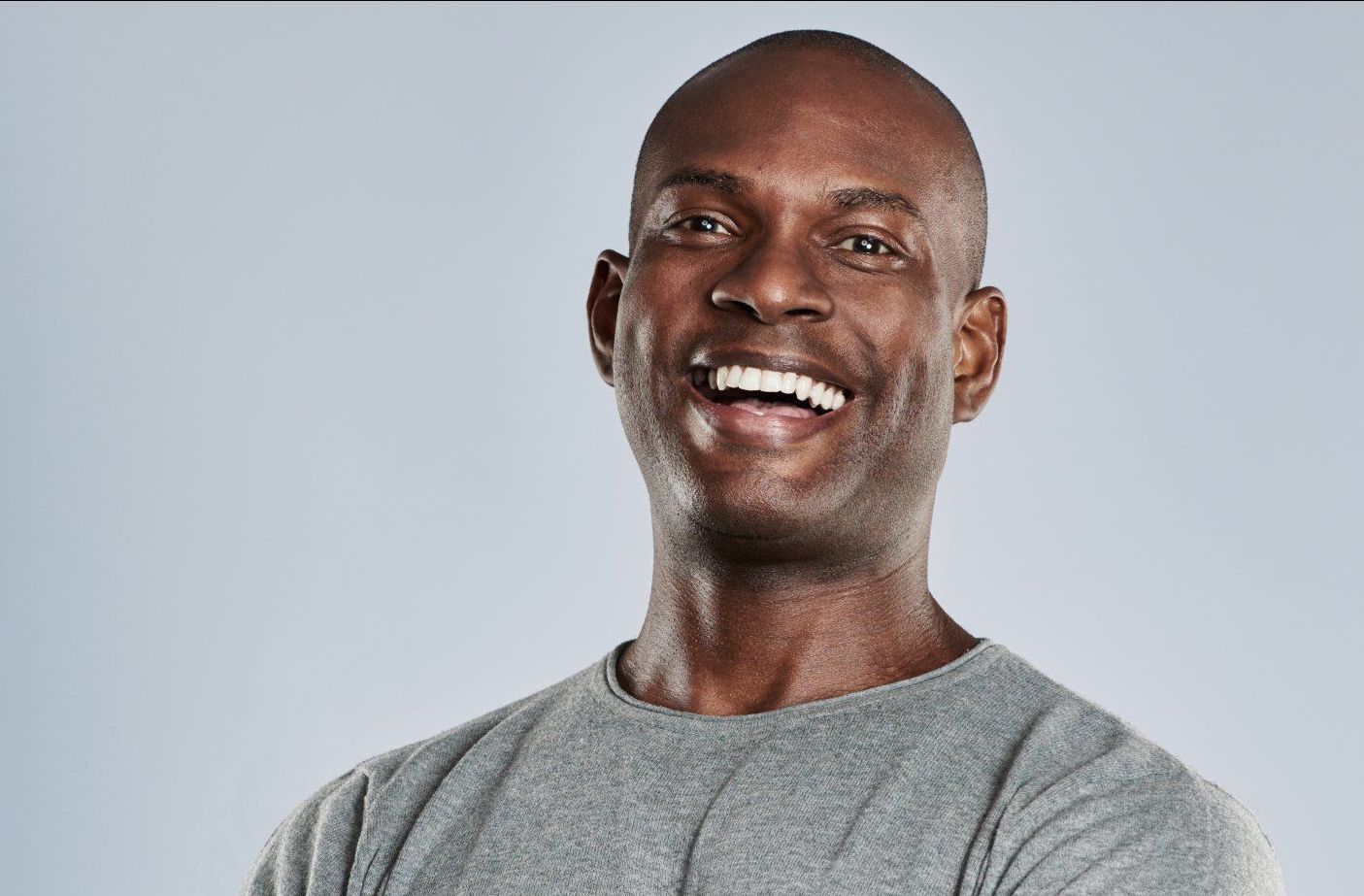 Man smiling, wearing a gray shirt, against a gray background.