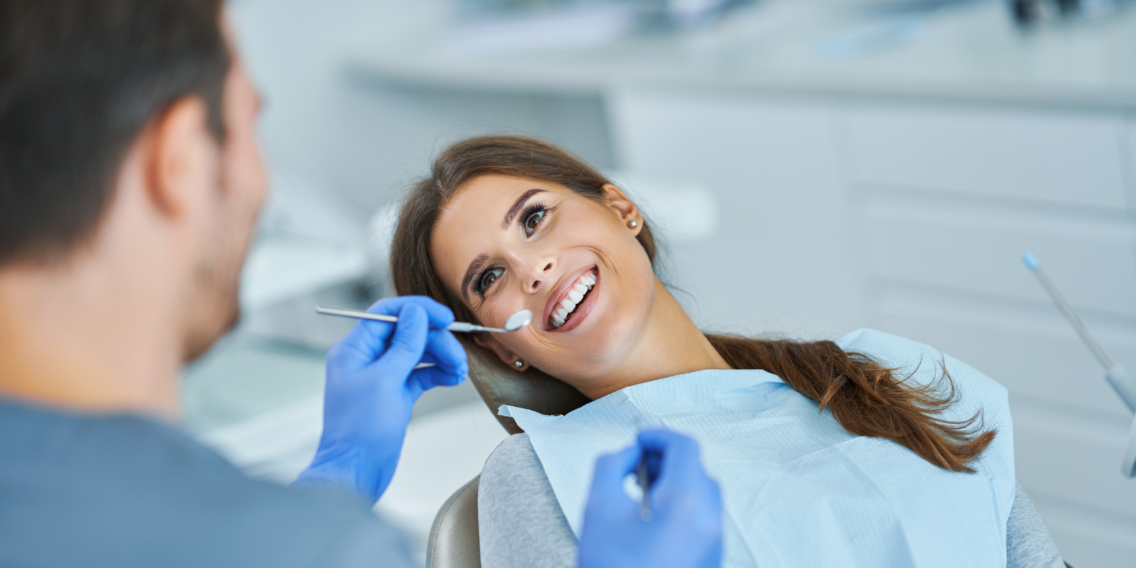 Dentist examining a smiling patient in a dental chair with blue gloves and tools