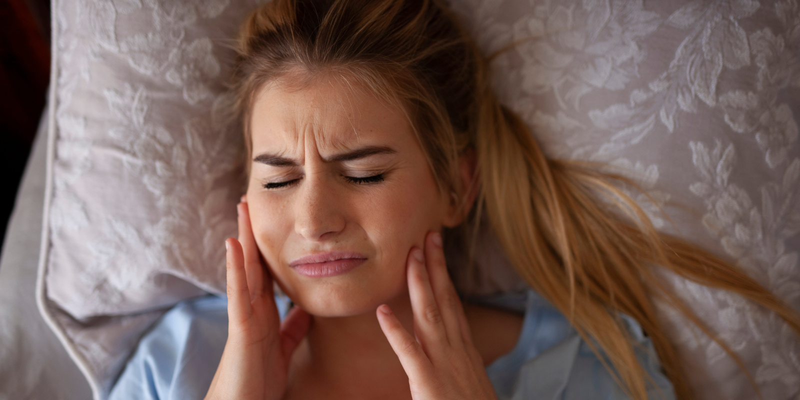 Woman holding her face with eyes closed, lying in bed and looking in pain or discomfort