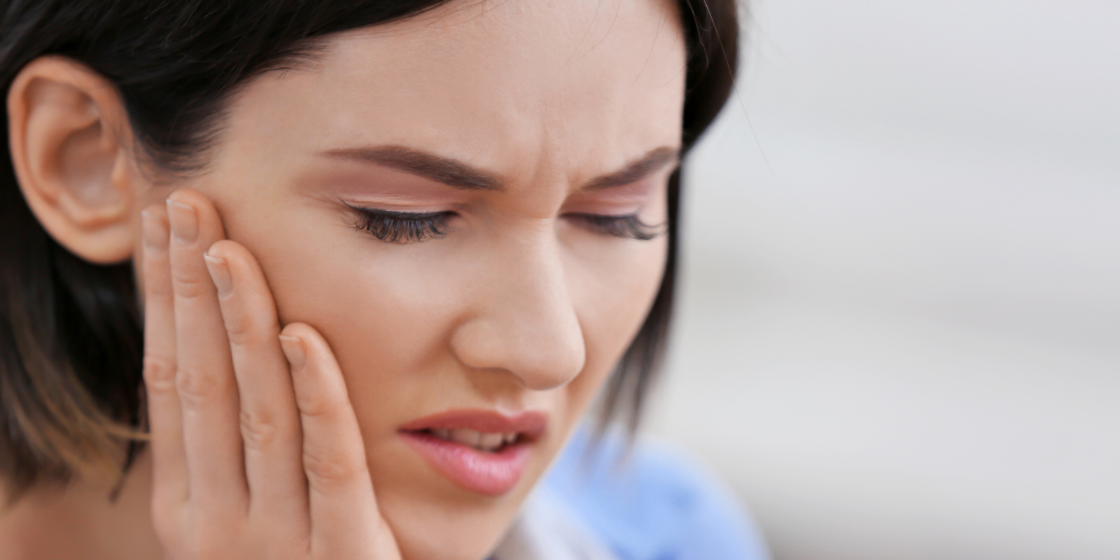 Person holding cheek with a pained expression, likely toothache, against a soft blurred background