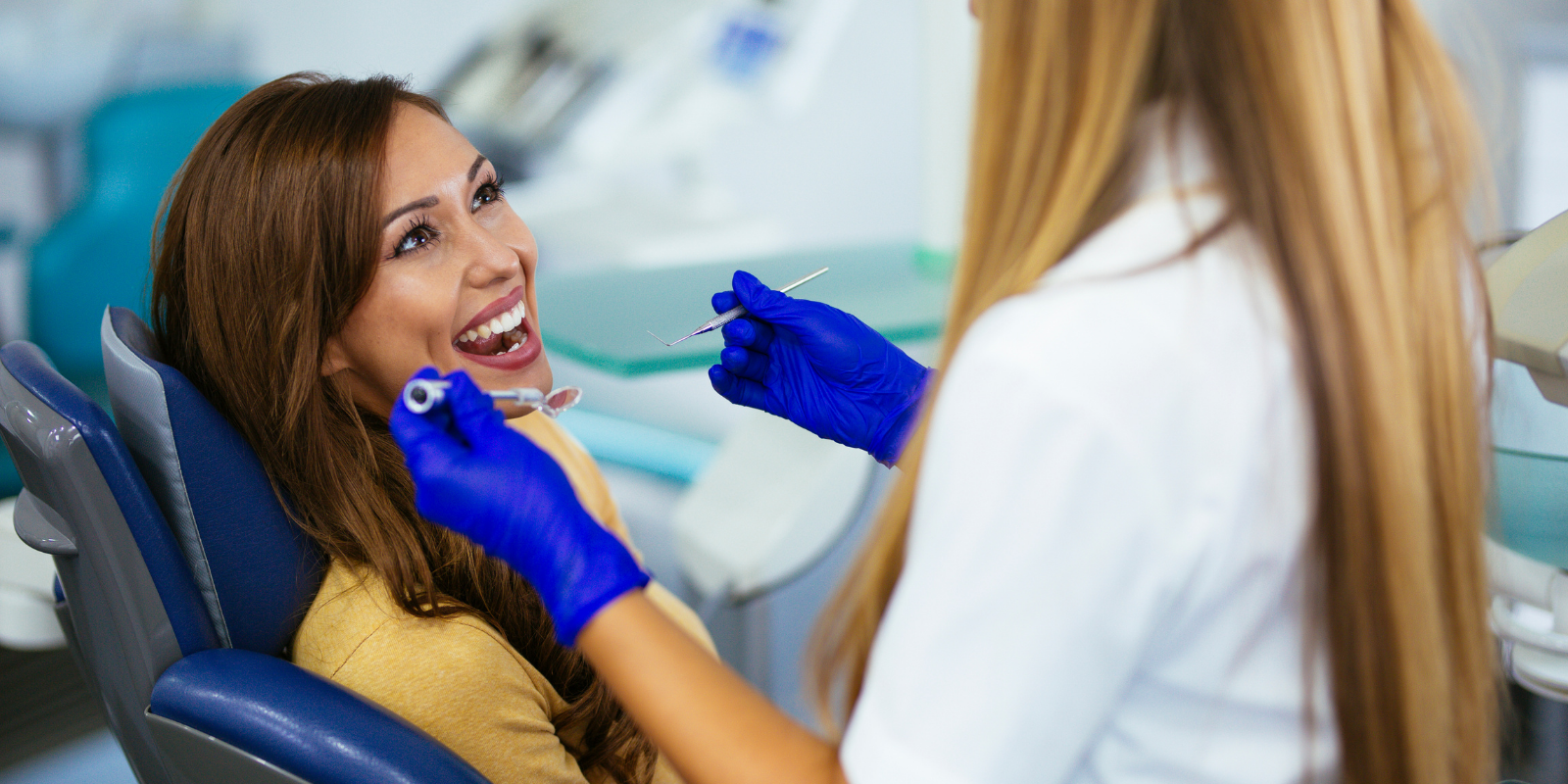Dentist examining a smiling patient’s teeth with blue gloves in a dental chair